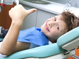 Young boy in dental chair giving thumbs up