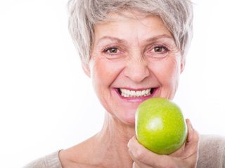 Woman with dentures eating an apple in Edison 