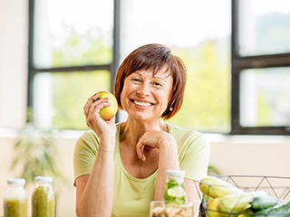 woman sitting in her kitchen and holding a green apple 