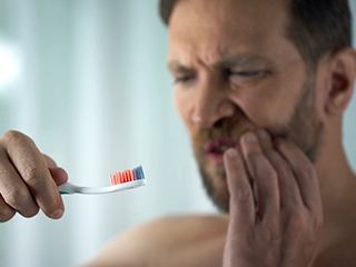Man with gum disease touches his cheek while looking at toothbrush with blood on it