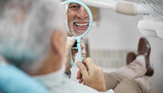 Older man smiling at his implant dentures in Edison