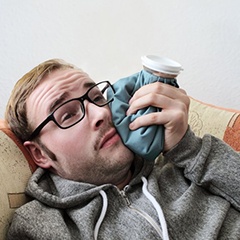 man lying on a couch and holding a cold compress to his cheek 