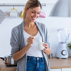 woman standing in her kitchen and eating yogurt 