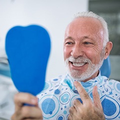 senior man admiring his smile after getting dental implant restorations placed 