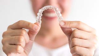 Woman smiling and holding out Invisalign in Edison