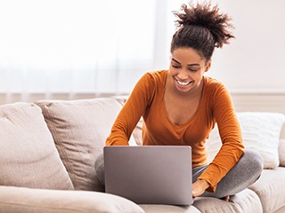 Woman smiling and sitting on couch using laptop