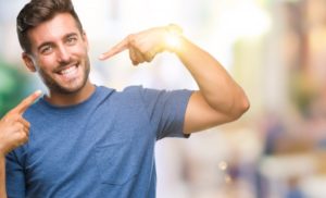 young man pointing to his smile after undergoing cosmetic dentistry 