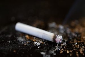 A lit cigarette butt laying on a table among ashes
