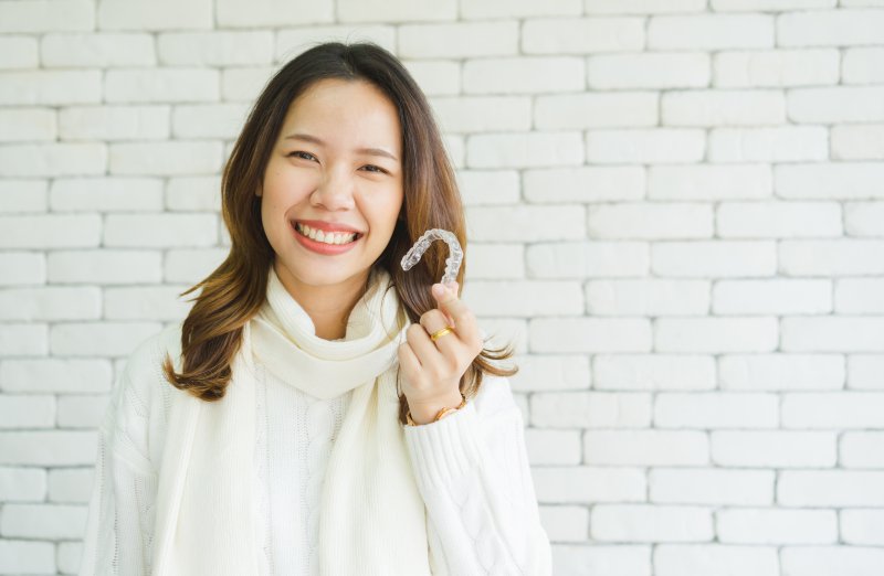 person holding Invisalign aligner and smiling