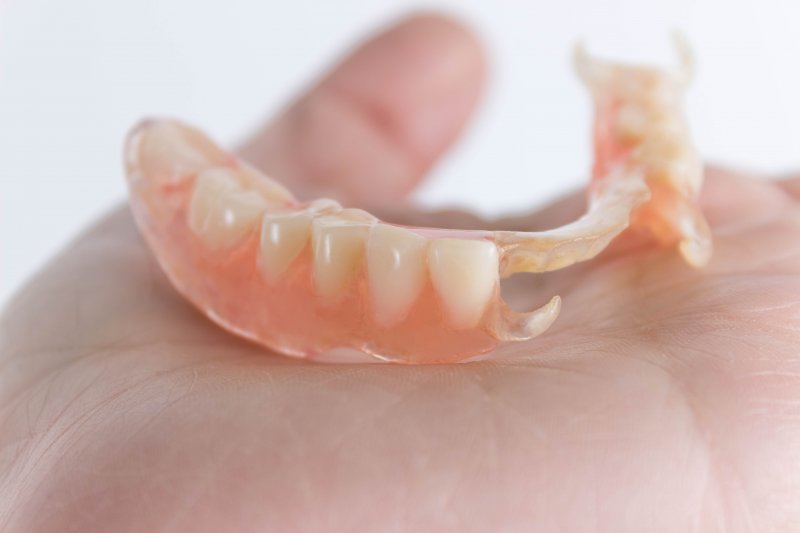 A partial denture sitting on the palm of someone's hand