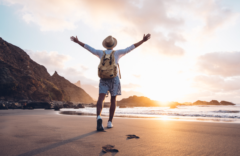 Traveler with backpack walking on beach towards sunset