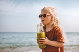 Child drinking smoothie from a glass bottle on the beach.