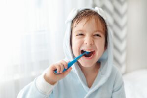 Little boy brushing his teeth and wearing a sweater.